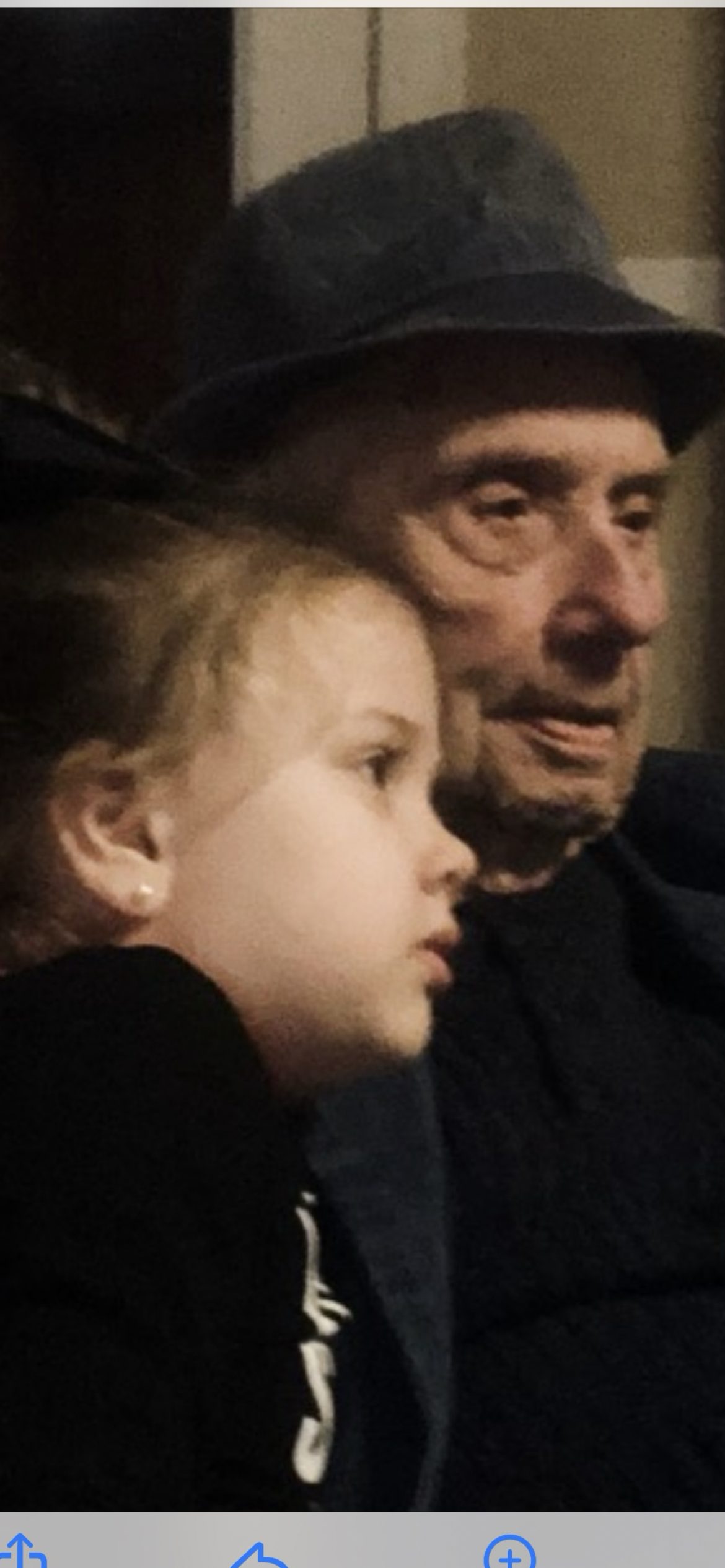 An elderly man and a young girl sit closely, enjoying each other's company at a family gathering.