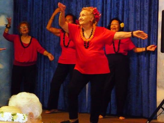 A lively group of senior women in red outfits dance joyfully at a community gathering.