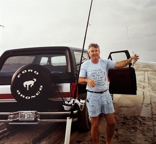 Fisherman poses with his catch near a vintage SUV parked on the sandy beach.