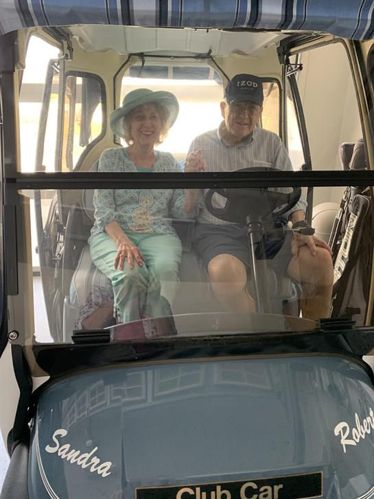A happy couple sits in a golf cart, smiling and enjoying their time together outside.