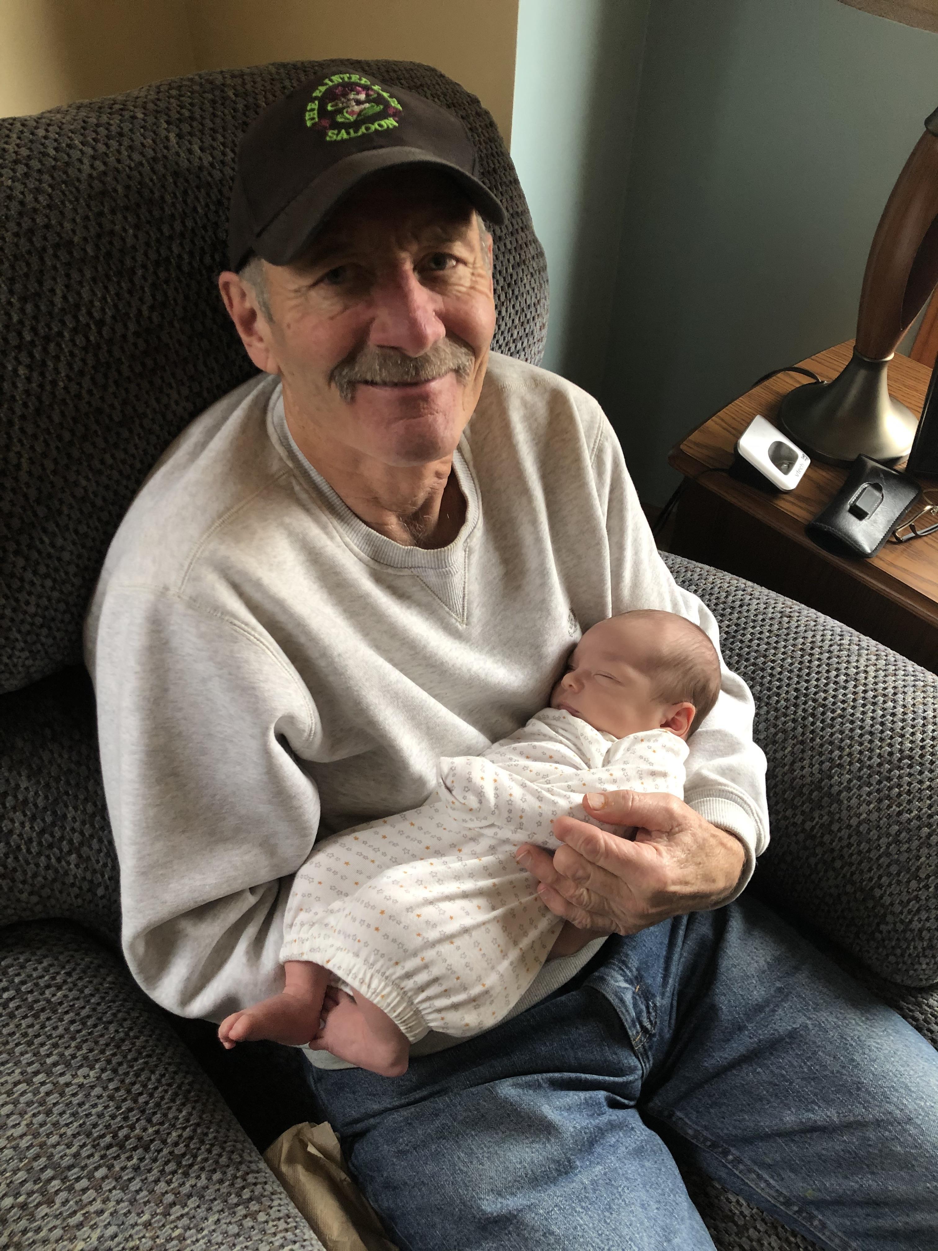 Elderly man smiles as he lovingly holds a peaceful baby in a comfortable chair.