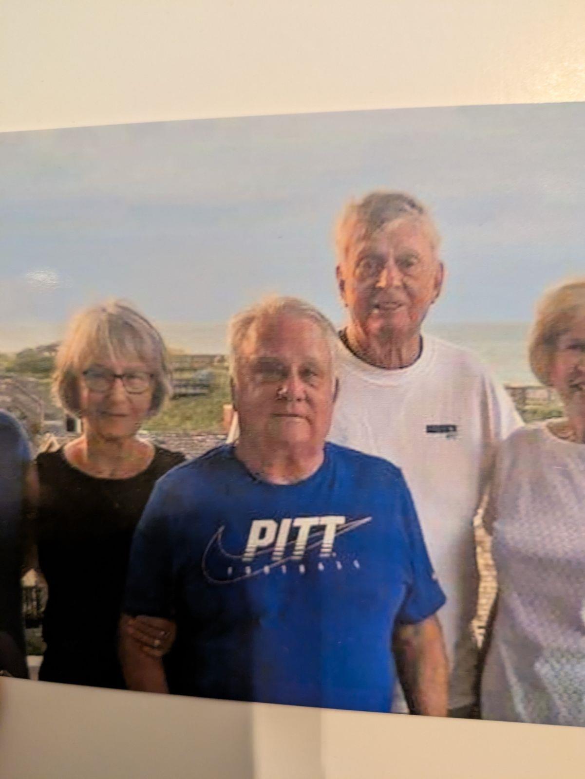 A group of five friends stands together, smiling warmly, with the ocean behind them.