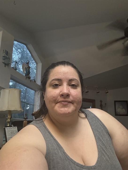 A woman poses for a selfie inside her home, with a cozy atmosphere visible through the window.