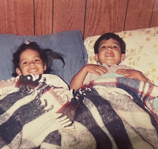 Two smiling children are snuggled in bed, wrapped in bright blankets, ready for sleep.