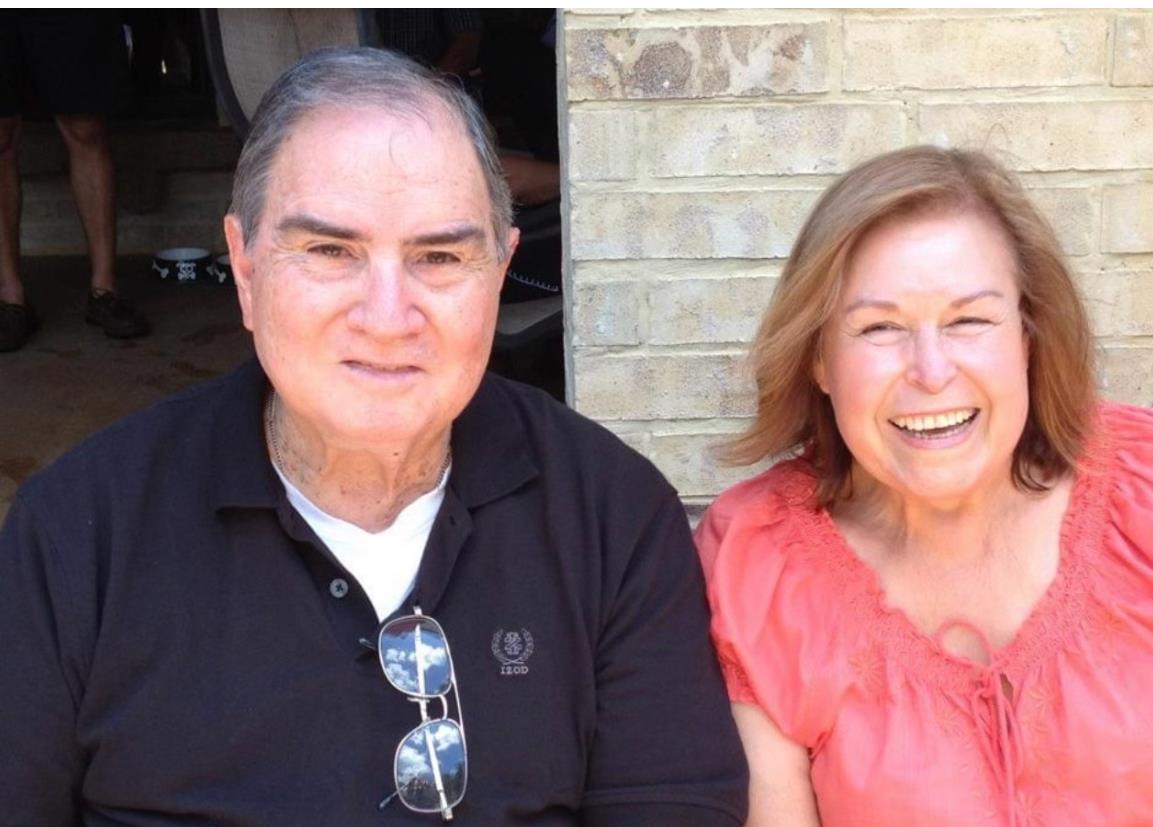 Elderly couple sits together, smiling warmly while enjoying each other's company outdoors.