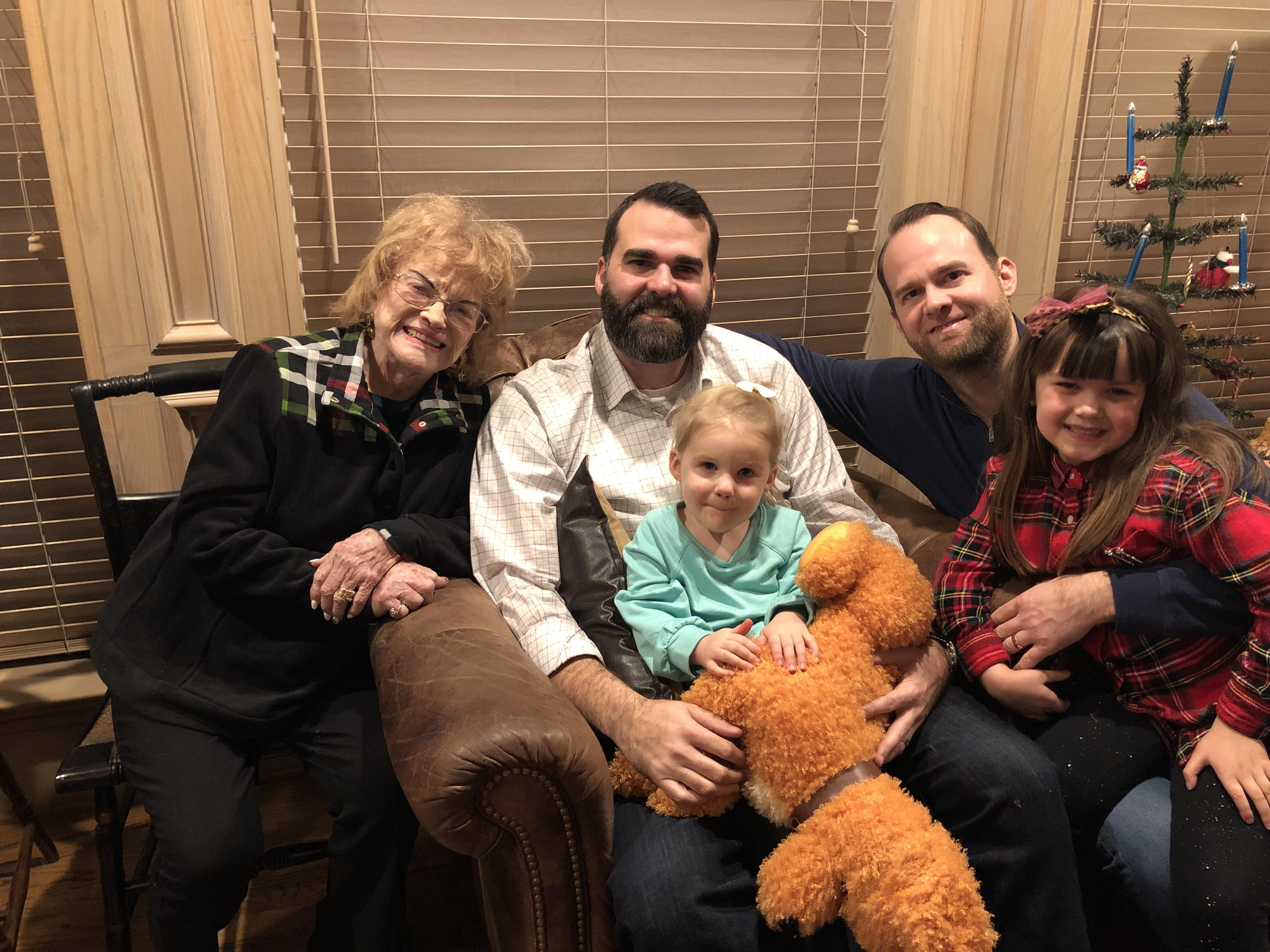 A family enjoys quality time on a couch, surrounded by smiles and cuddly toys in a cozy space.