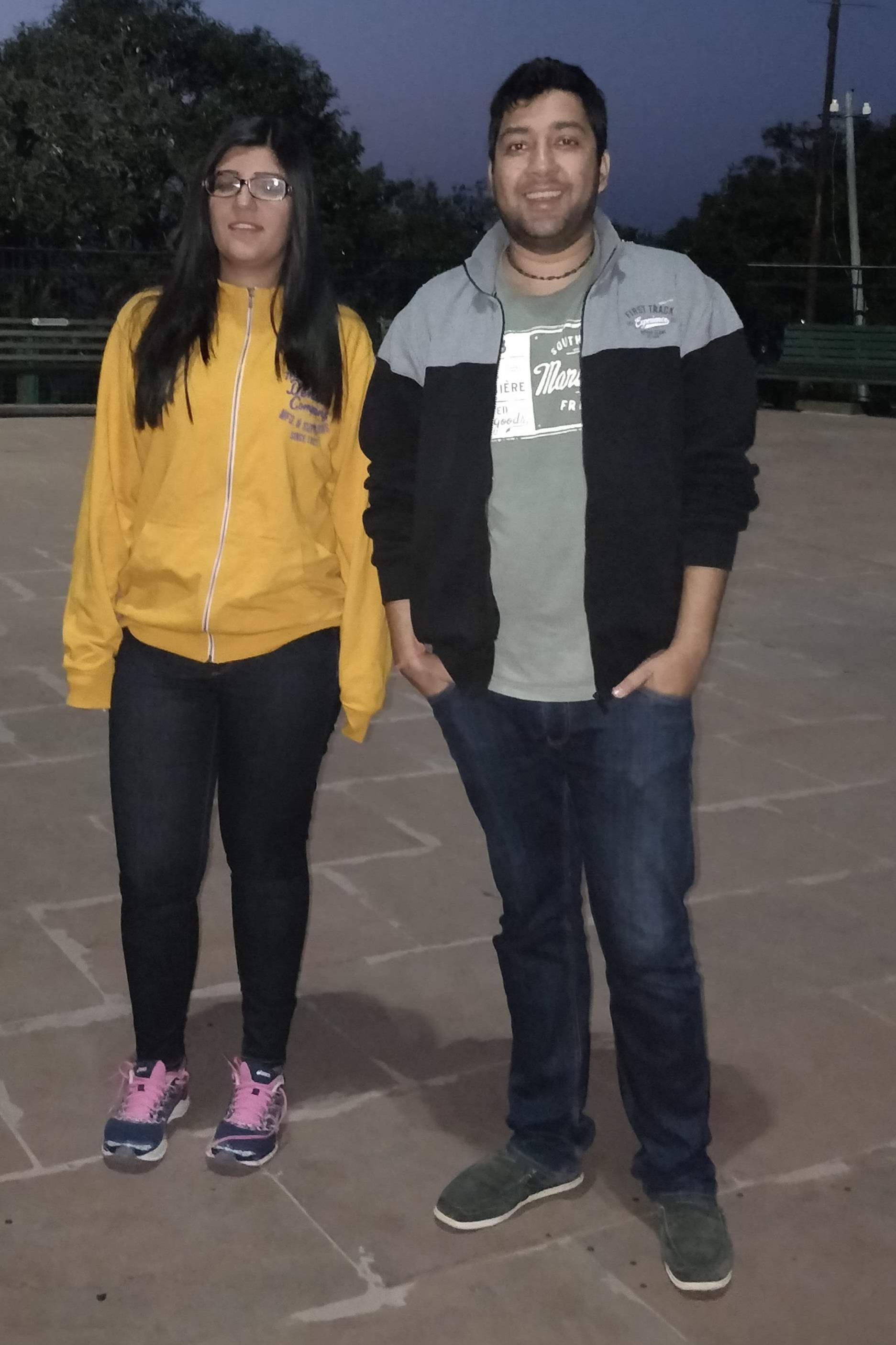 Two young adults stand together in a park as evening approaches, enjoying the moment.