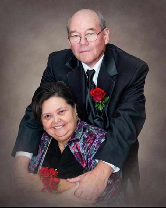 A couple in formal attire embraces with red roses, celebrating their love and joy.