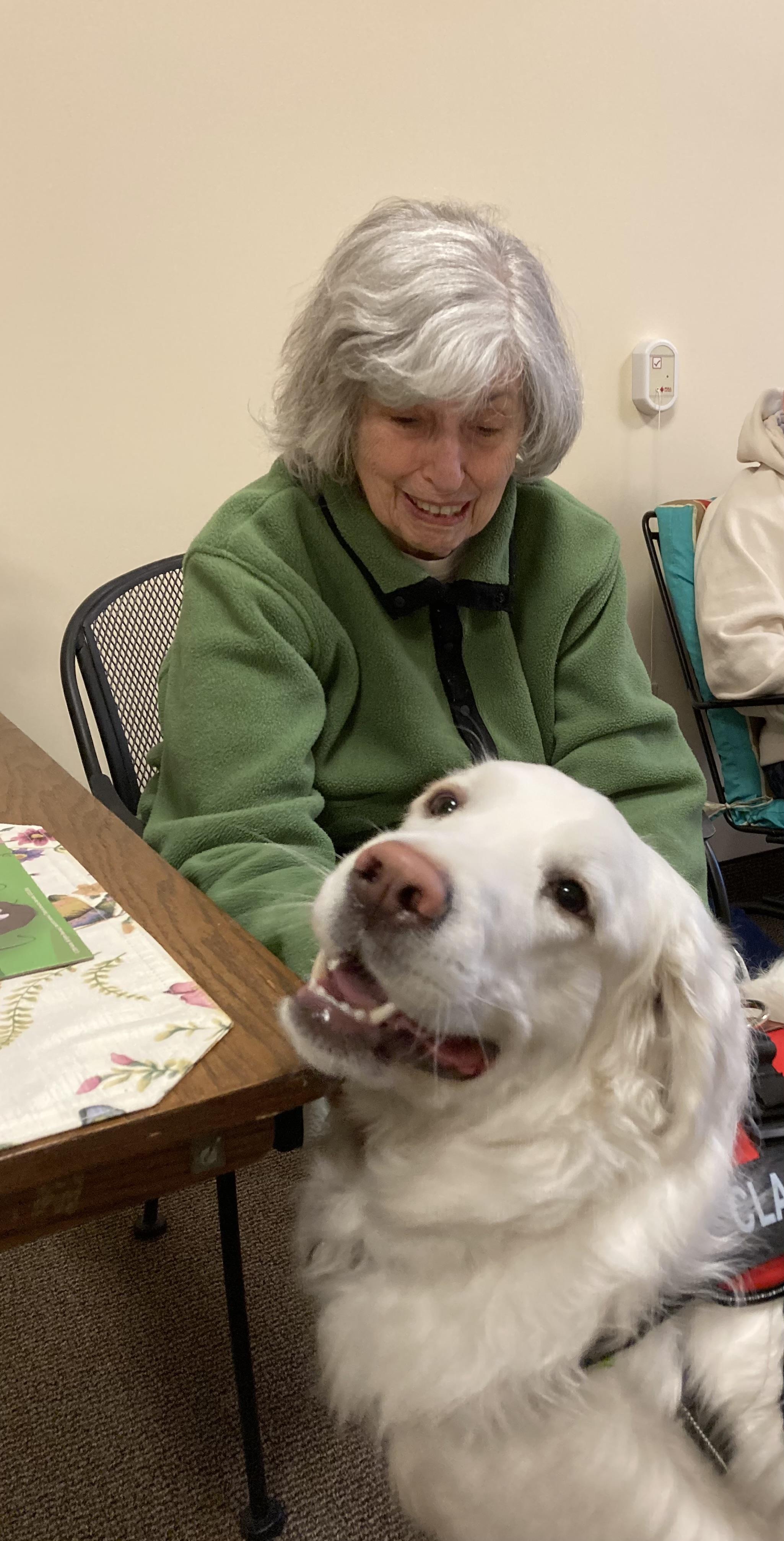 An elderly woman enjoys playful moments with a golden retriever in a community center.