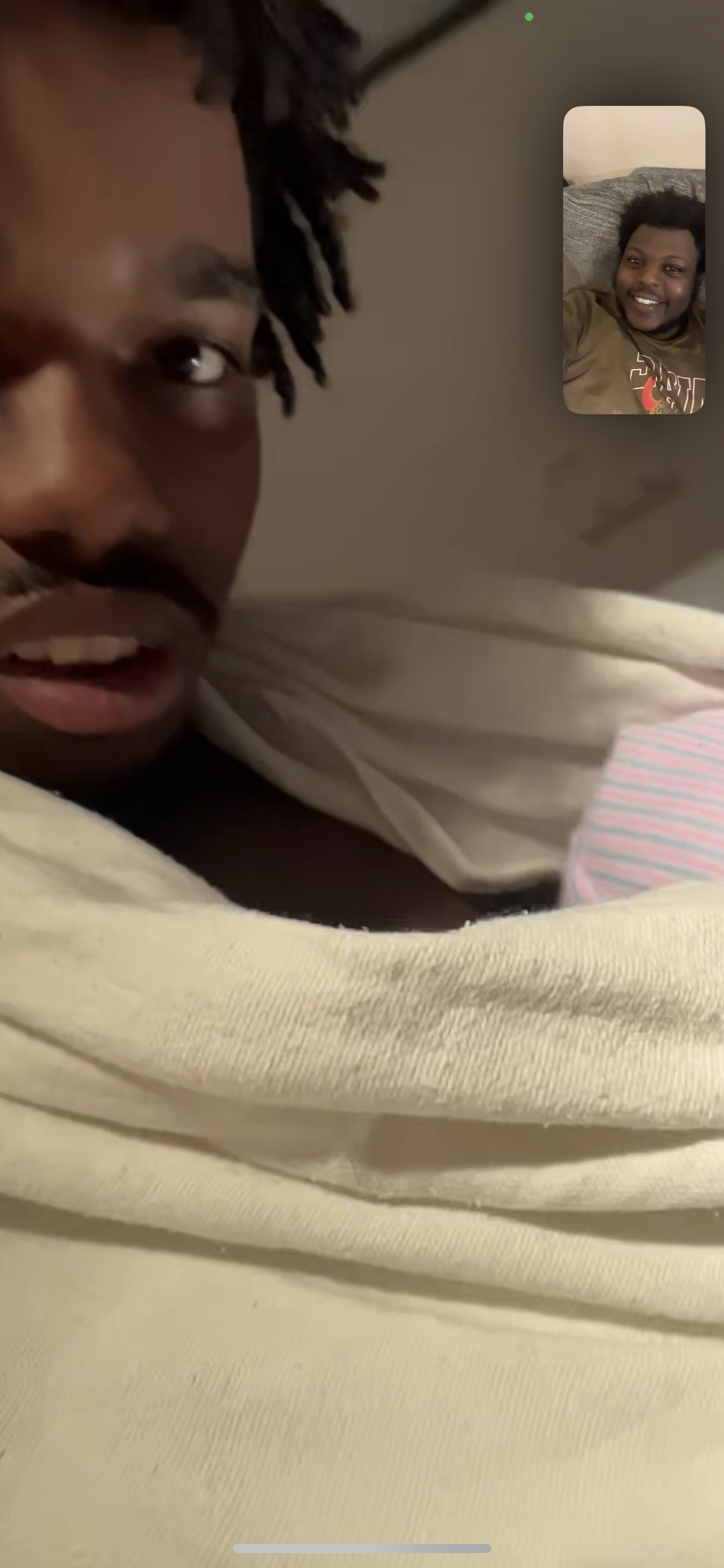 A young man is engaged in a video call, wrapped in a soft blanket at home.
