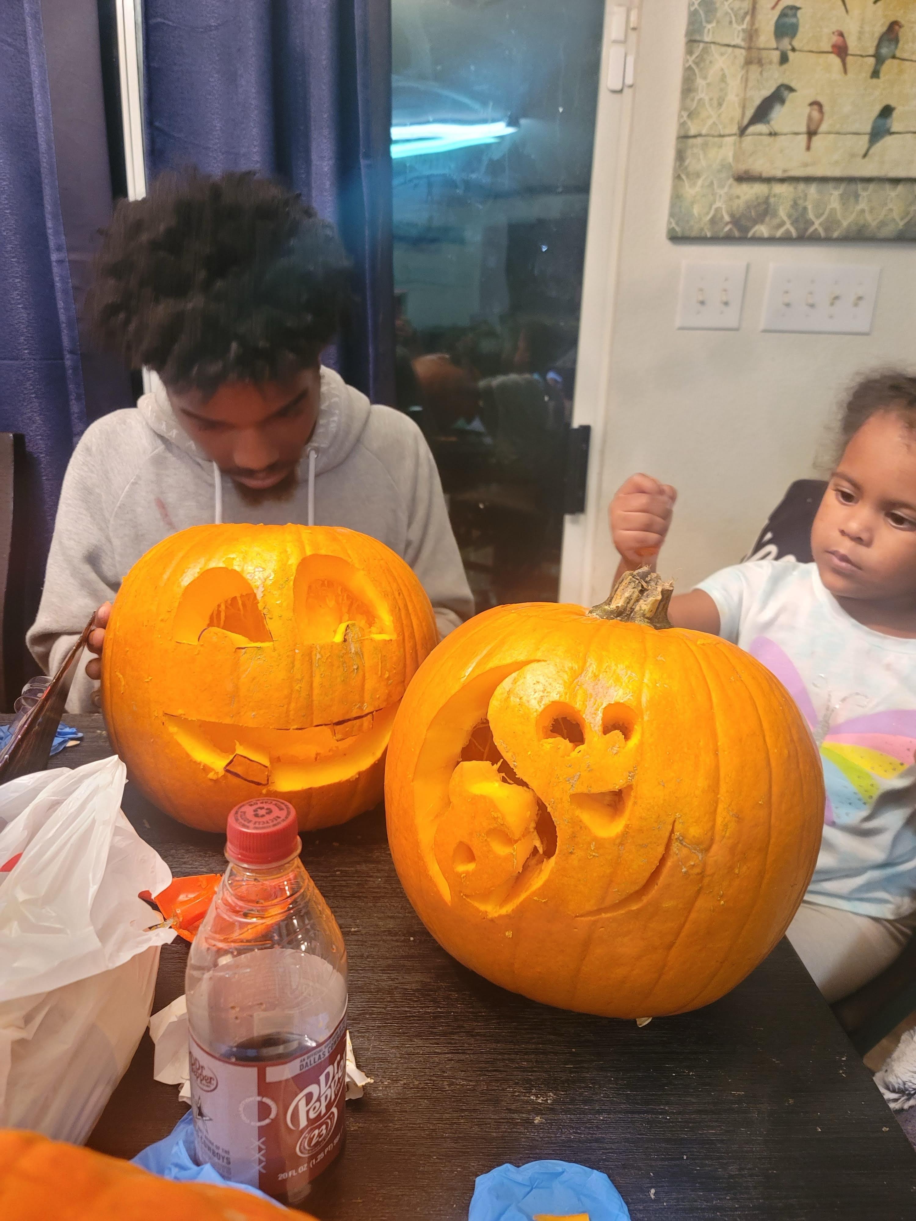 A child and an adult are carving pumpkins together, enjoying Halloween crafts indoors.