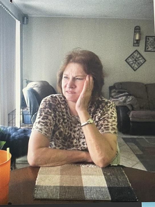 A woman rests her chin on her hand, looking thoughtfully while seated at a table.
