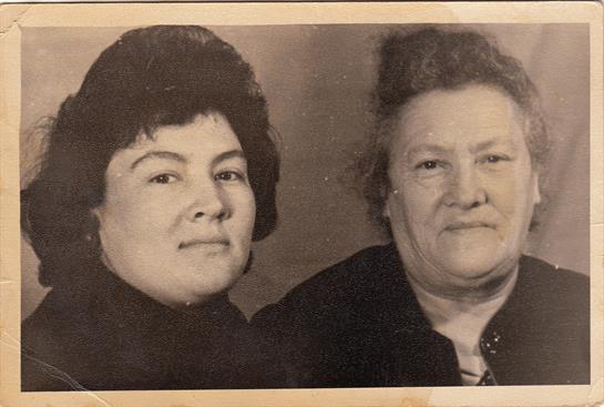 Two women pose closely, smiling gently, exhibiting a strong connection from their past.