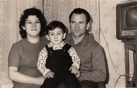 Parents sit with their child in a cozy living room with vintage decor, capturing a moment of joy.
