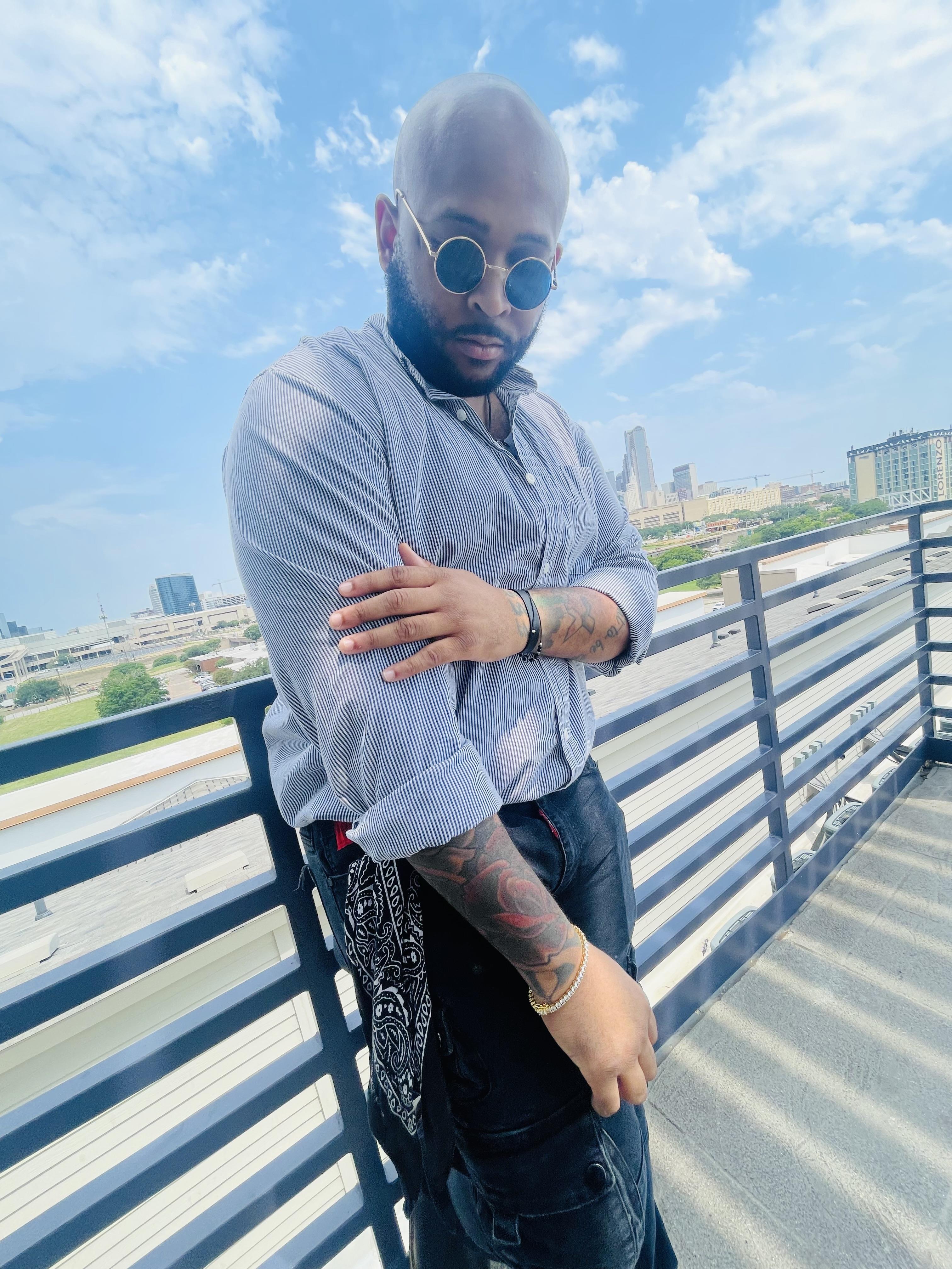 A man dressed in a stylish outfit poses confidently on a rooftop with a city view.