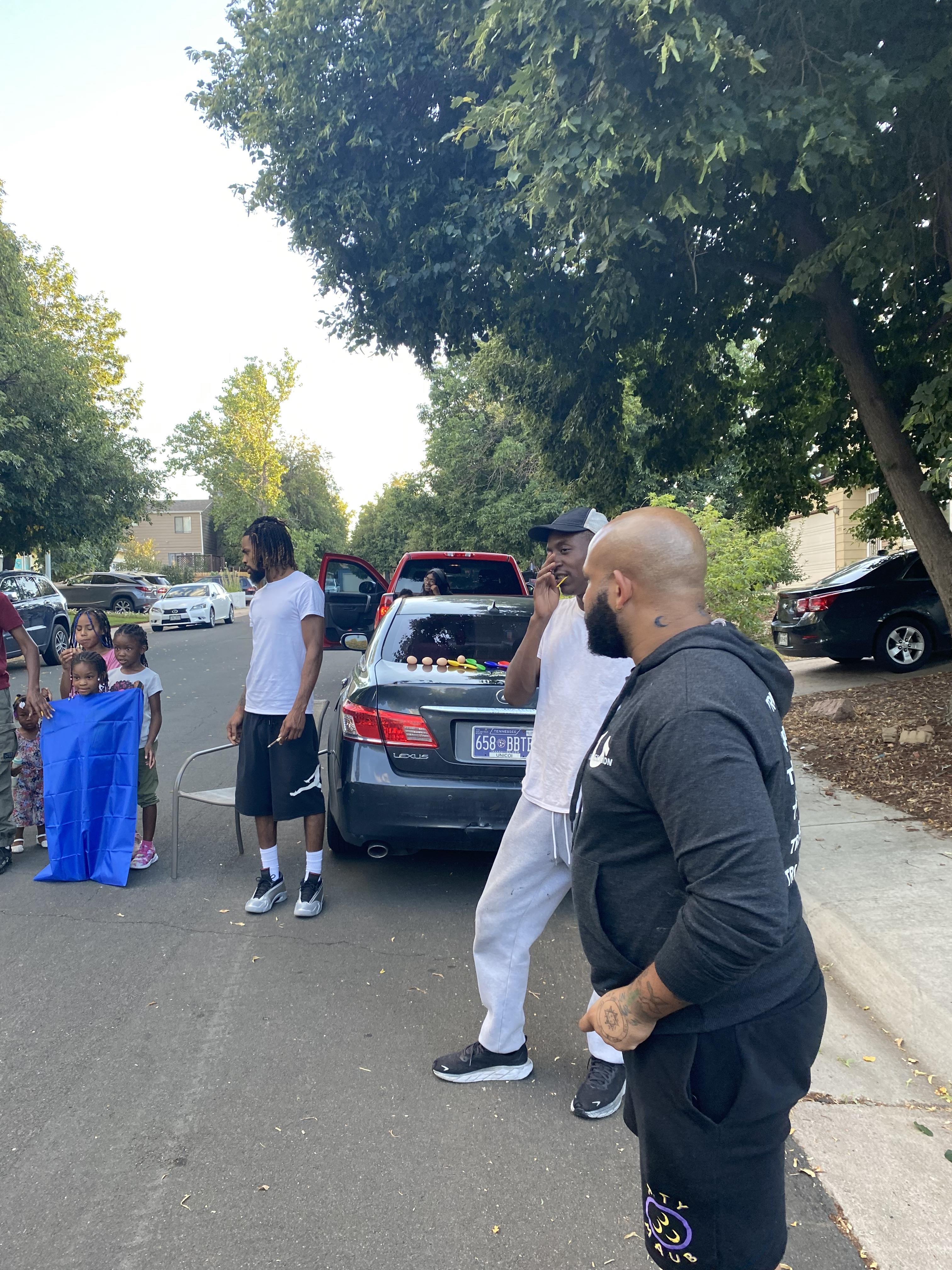 Families and friends enjoy outdoor activities and socializing on a warm day in a residential area.