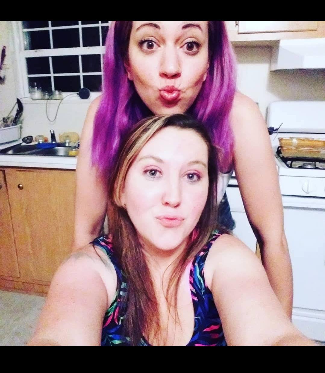 Two friends pose playfully in a bright kitchen, showcasing their camaraderie and fun spirit.