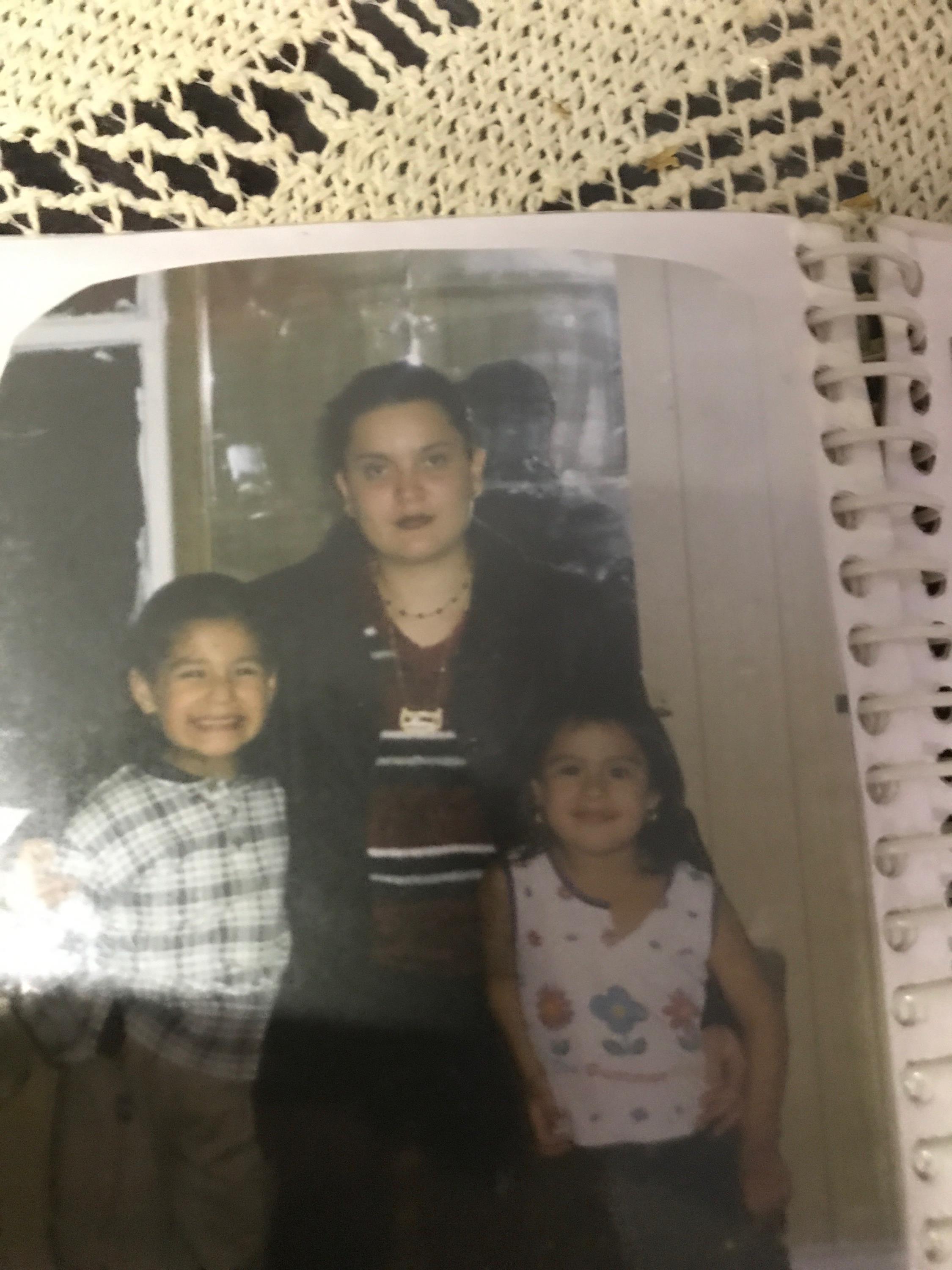 A mother stands proudly with her two cheerful children in a warm indoor atmosphere.