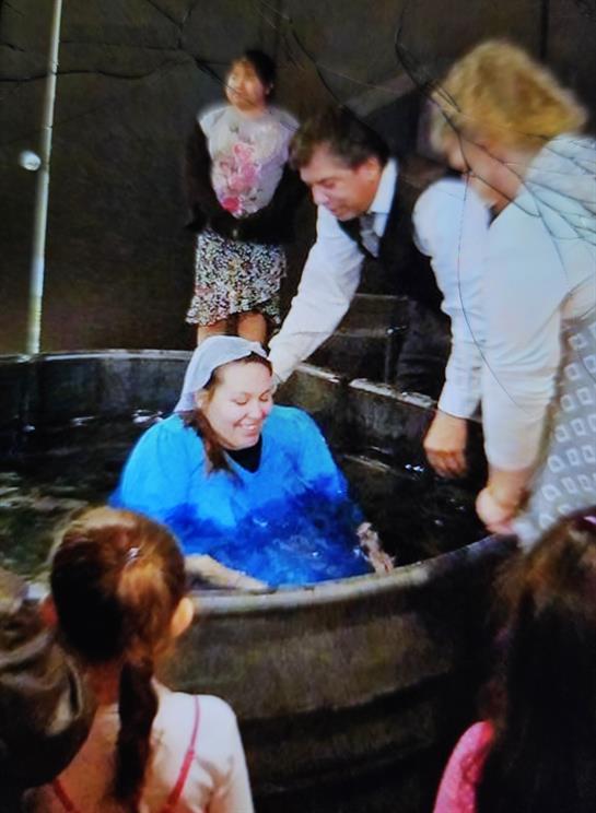 A woman is being baptized in a large tub while friends and family watch with support.