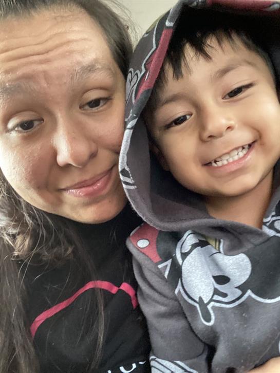A woman and her young son enjoy a happy moment together, smiling cheerfully at the camera.