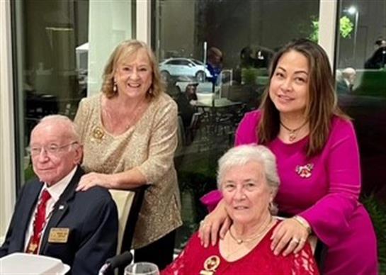A group of four friends poses happily at a festive gathering in a well-lit venue.