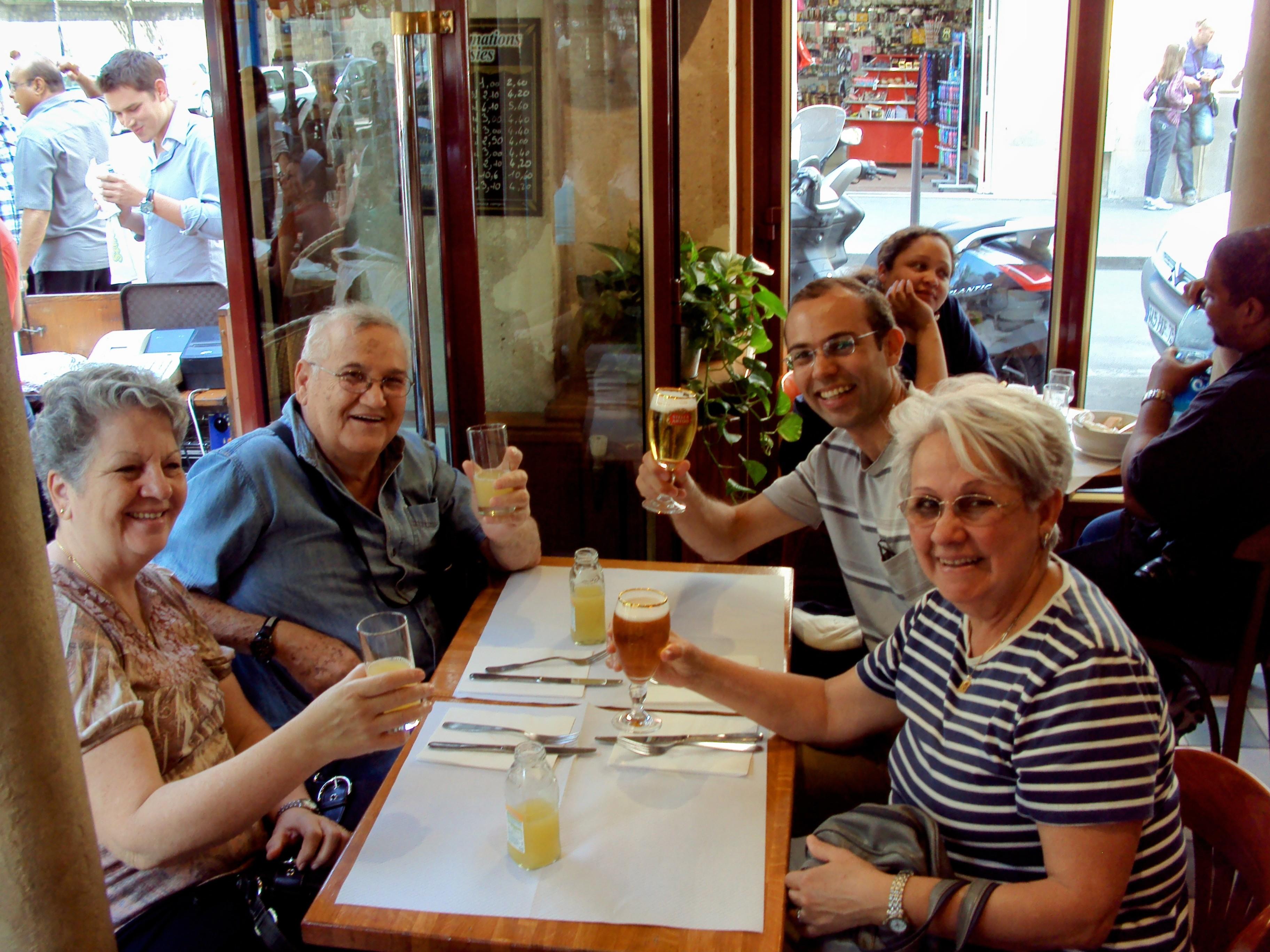 Group of four friends cheerfully raising glasses at a cafe in a bustling street.