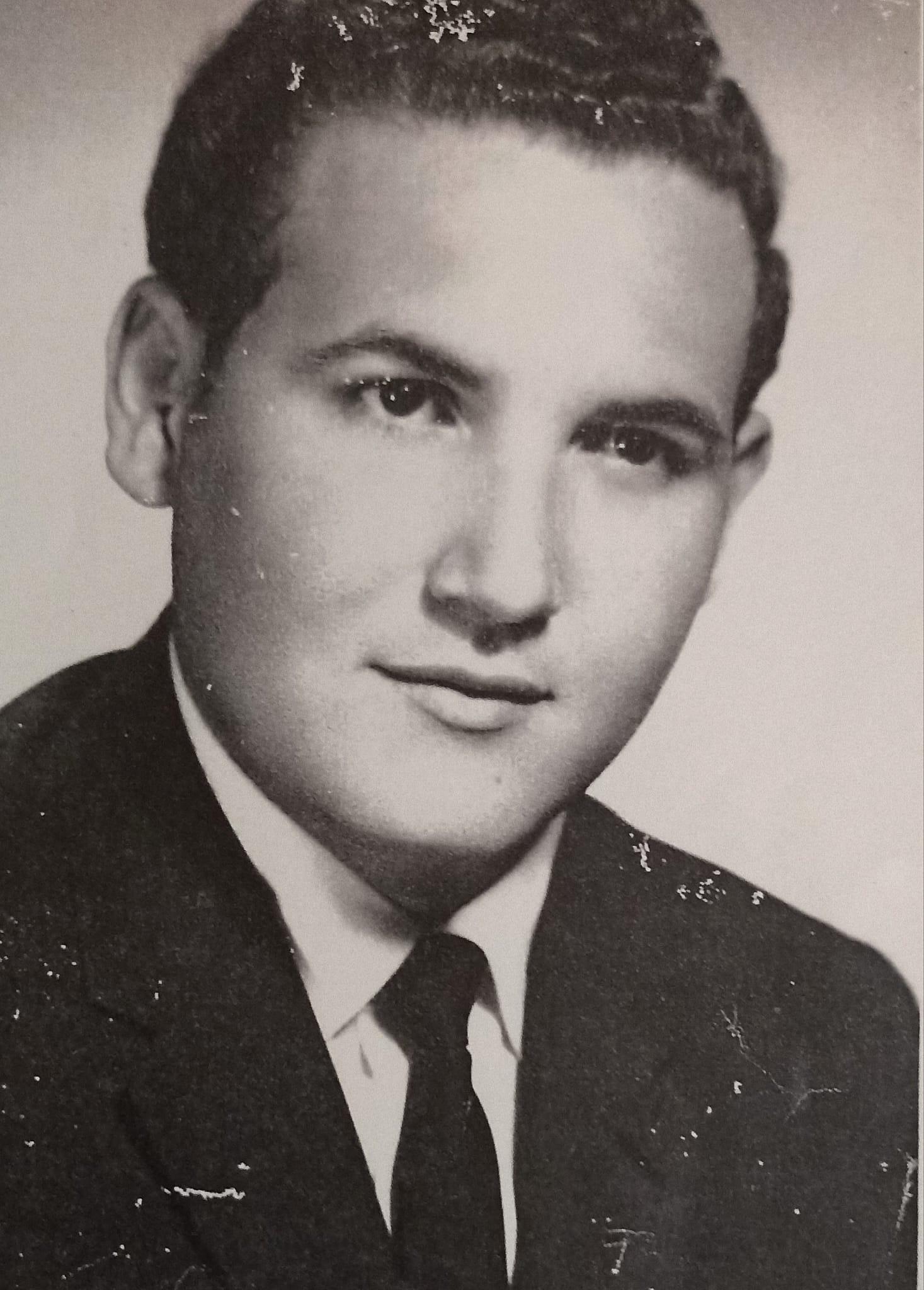 A young man poses in formal clothing, showcasing a confident expression and classic hairstyle.