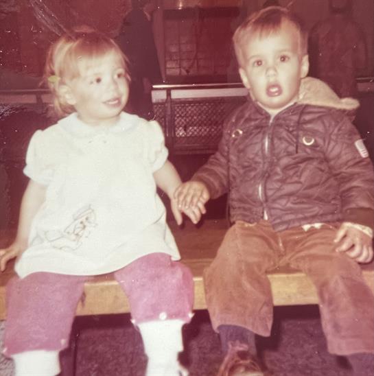 Young boy and girl share a moment holding hands while seated on a bench indoors.