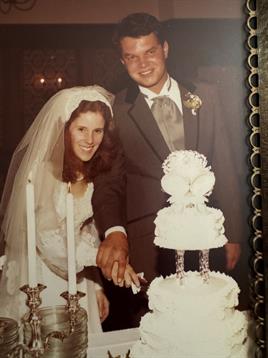 A joyful couple in formal attire cuts a wedding cake decorated elegantly, surrounded by candles.