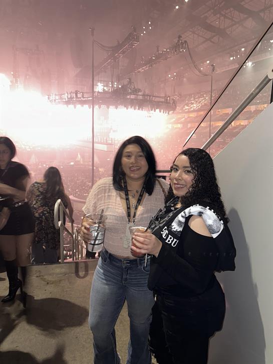 Friends pose with drinks in hand, enjoying a lively concert atmosphere at an arena venue.