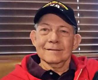 Older man with a warm smile, dressed in a red jacket, enjoys time with friends indoors.
