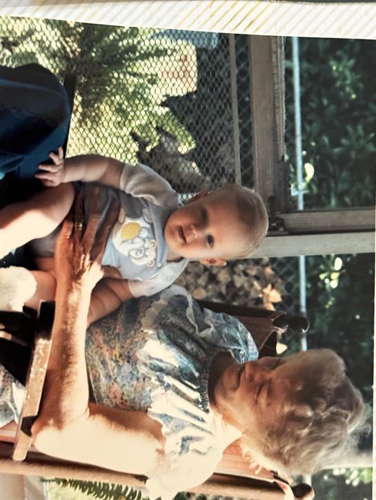 A grandmother holds her happy grandchild in a garden while enjoying quality time together.