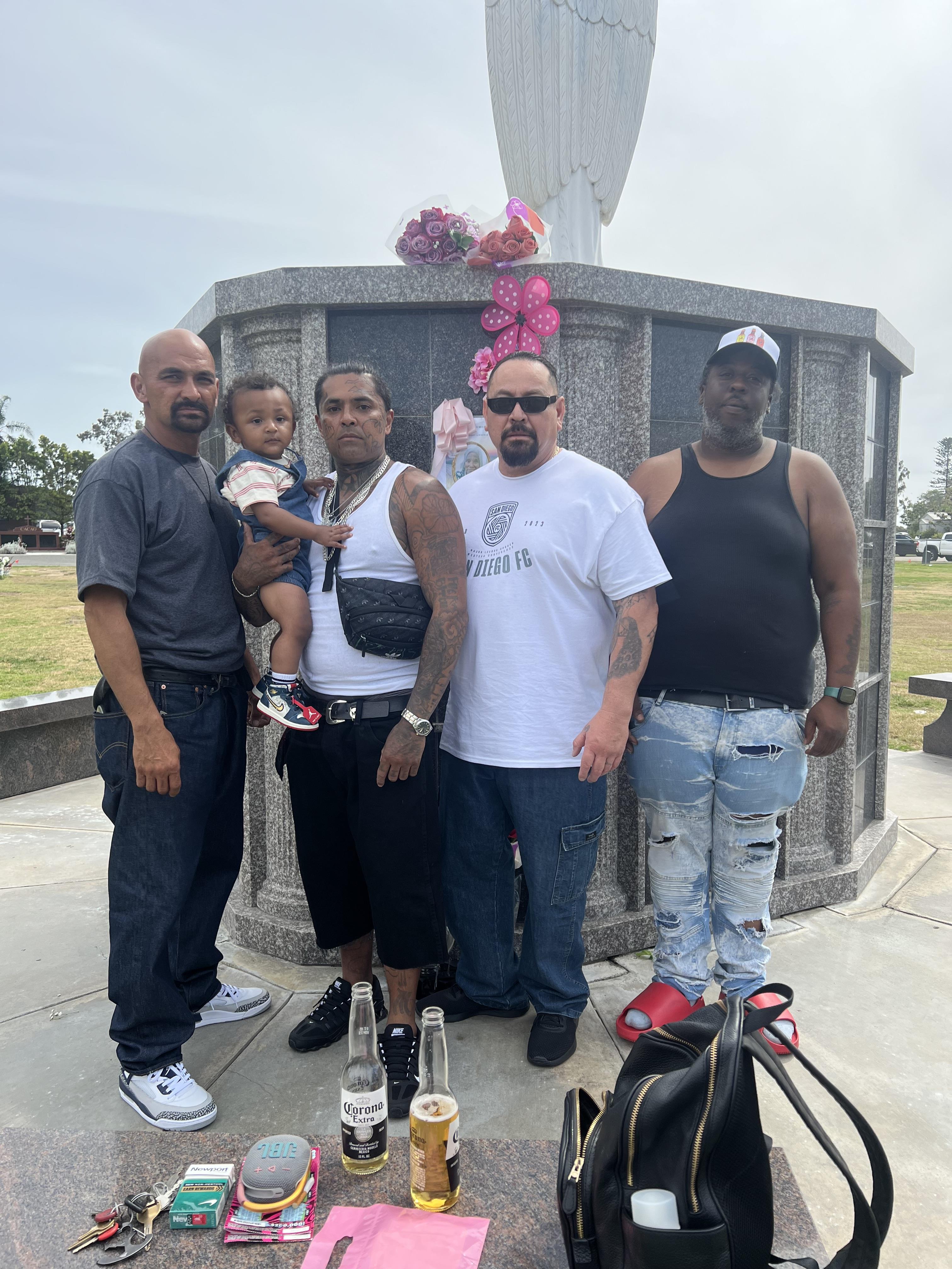 Four family members pay tribute to a loved one at a memorial adorned with flowers and belongings.