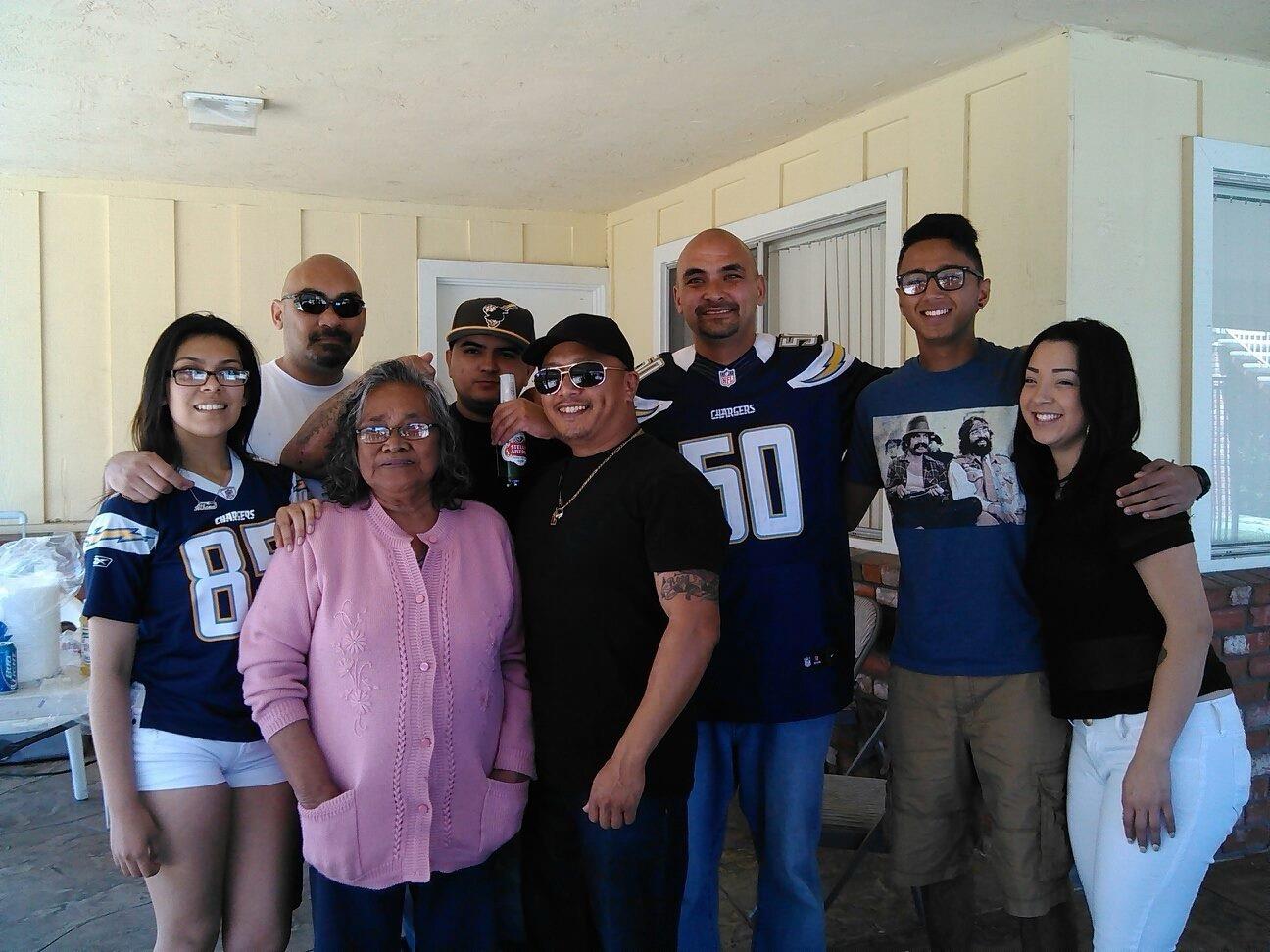 Family members gather outdoors in the backyard, wearing jerseys and enjoying each other's company.