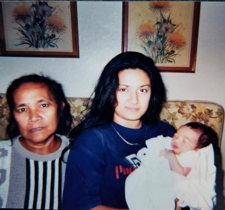 A proud mother holds her newborn baby while sitting beside her own mother in a welcoming home.