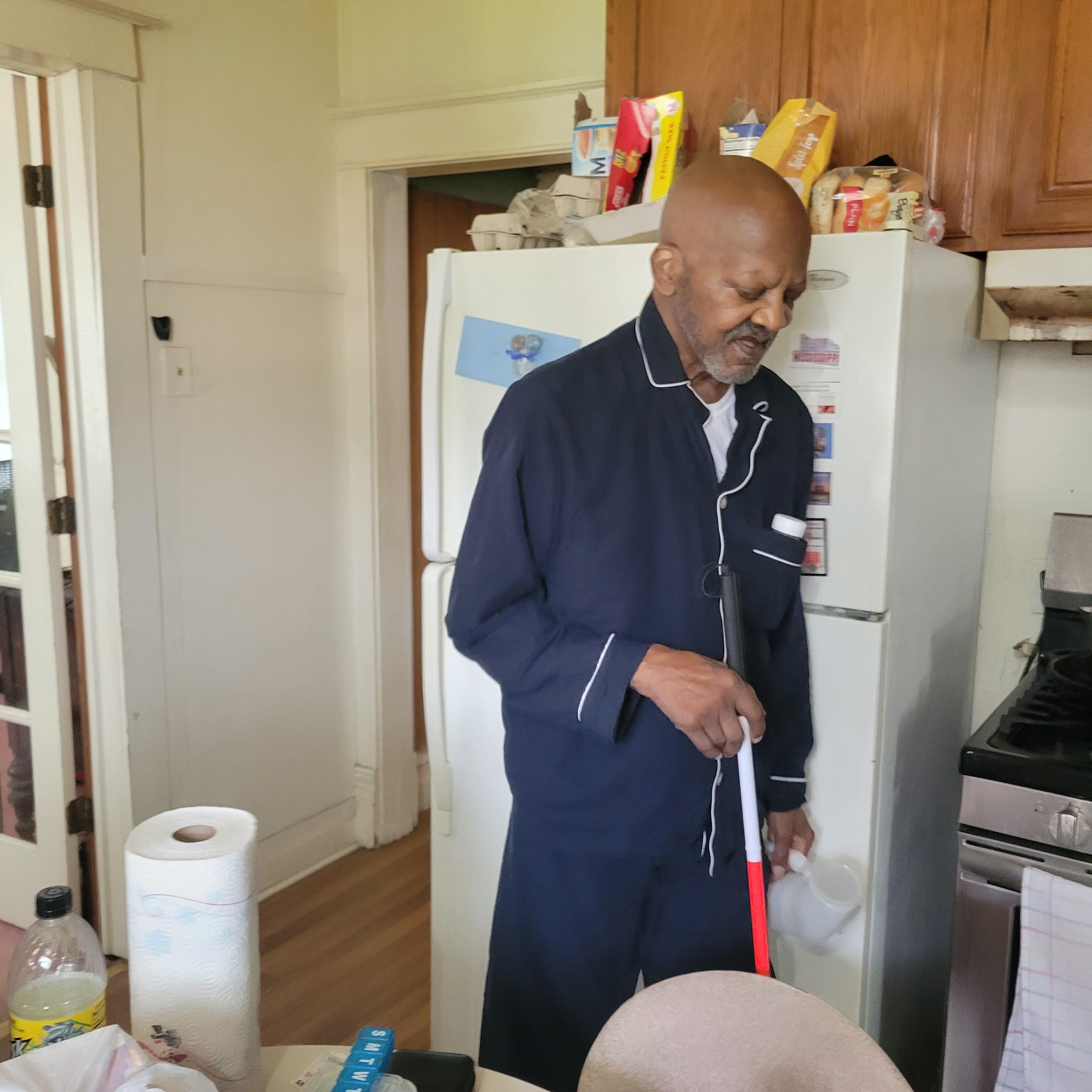 A man in a navy robe stands in a kitchen, arranging items as he prepares food for cooking.