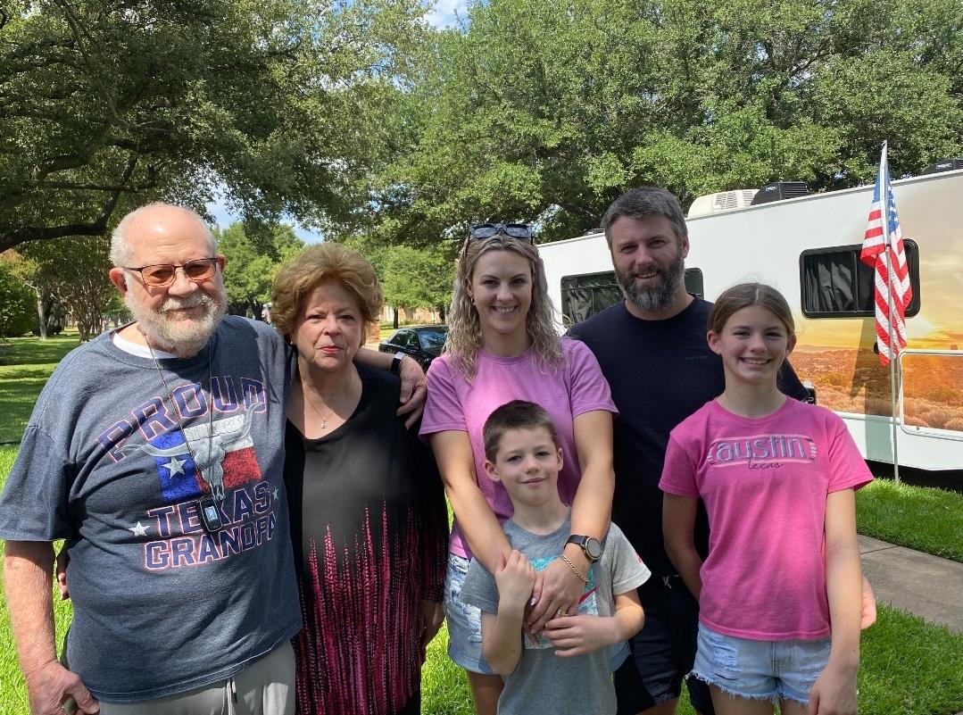 Family members smile together outdoors near their RV on a bright sunny day.