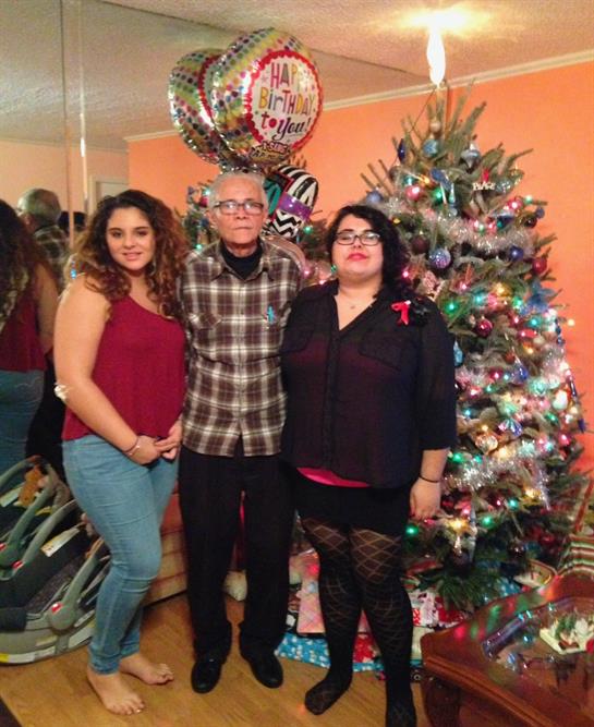 Group of three people posing happily in front of a colorful Christmas tree during a celebration.