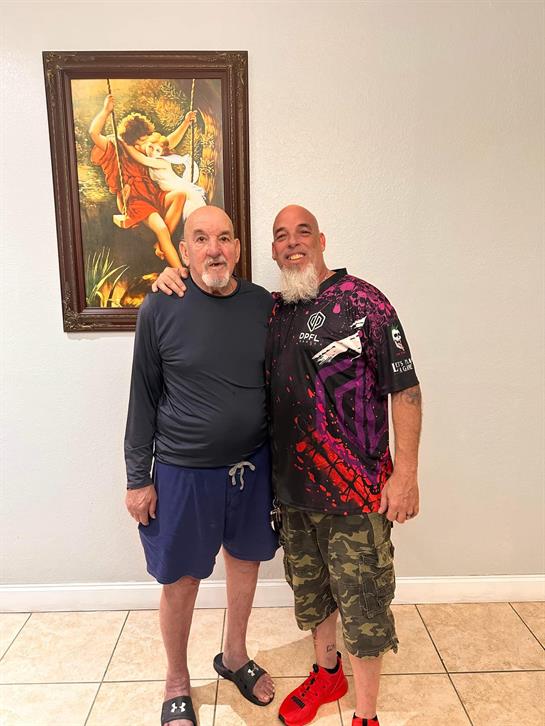 Two men pose for a photo in a light-filled room, engaging in friendly conversation and laughter.