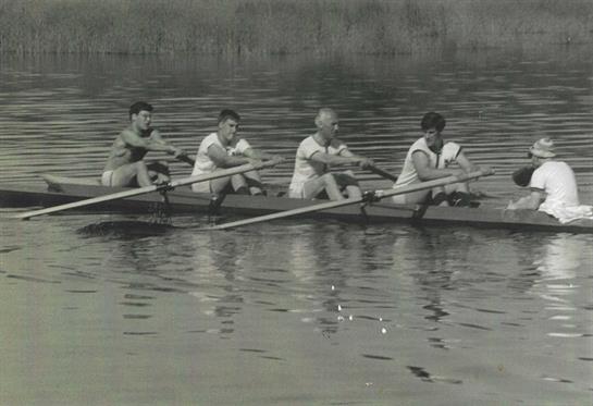 A group of five rowers engage in practice on a serene body of water at dawn.