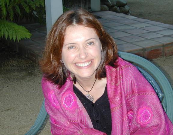 A woman enjoys a sunny day sitting outside, wearing a colorful shawl and smiling happily.