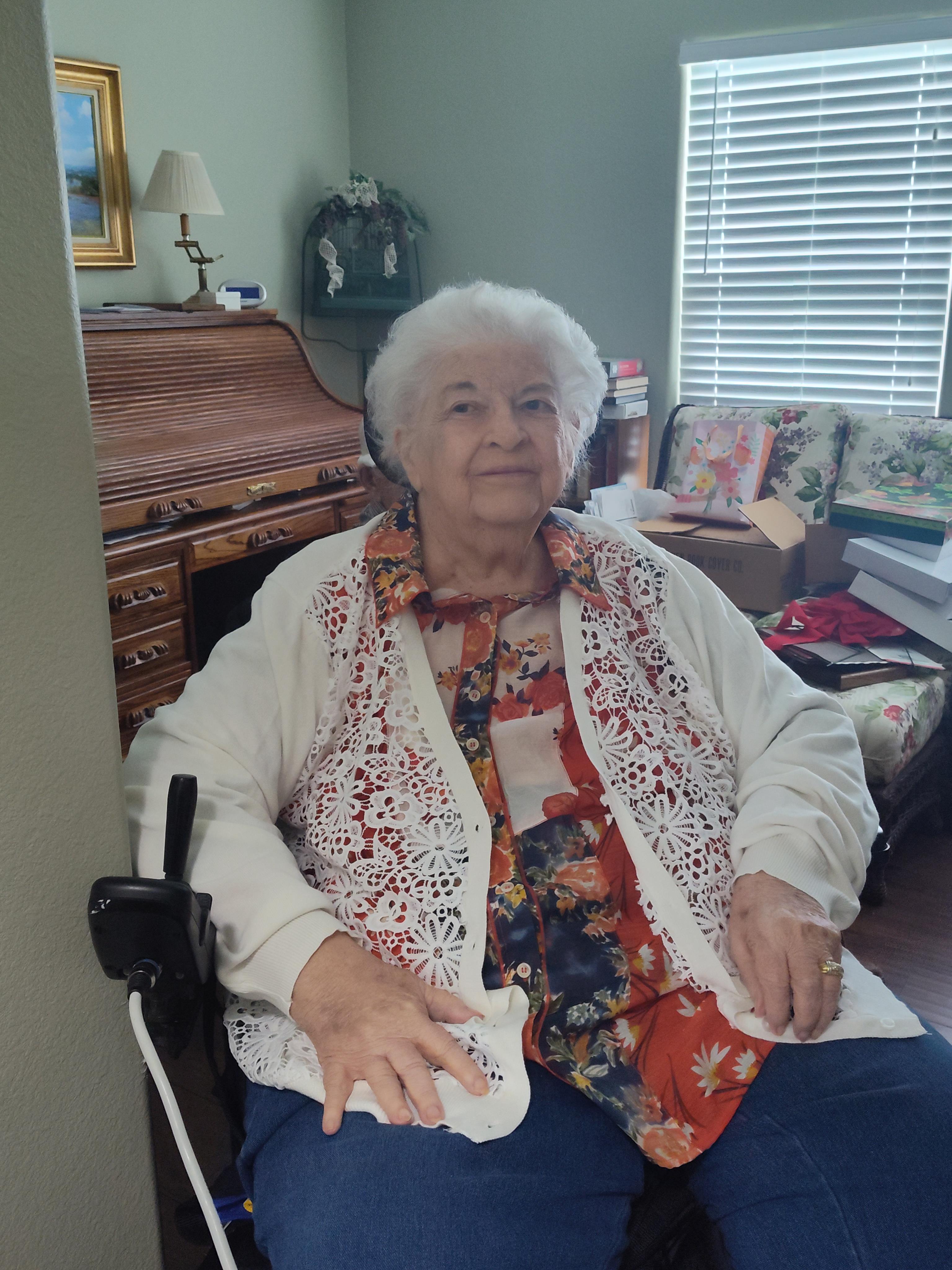 An elderly woman relaxes in her living room, surrounded by personal items and natural light.