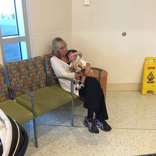 A woman embraces a child with a stuffed toy while seated in a waiting area, conveying comfort.