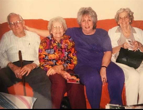 Four elderly individuals gather on a couch, sharing laughter and stories in a warm atmosphere.