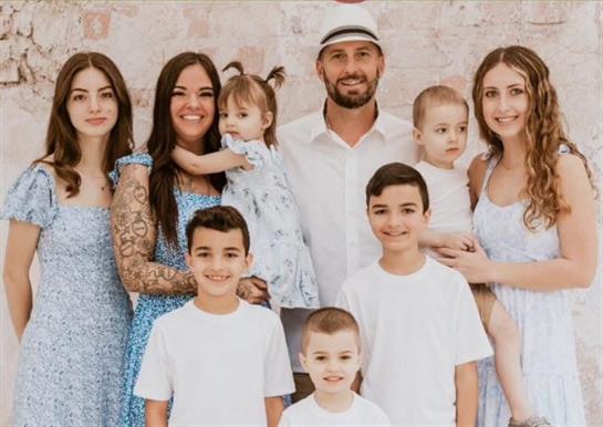 A happy family in light summer clothes poses with smiling adults and children.