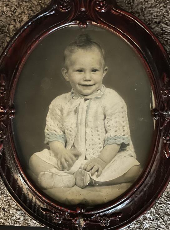 A joyful child in a vintage outfit smiles, sitting cross-legged in a classic frame.