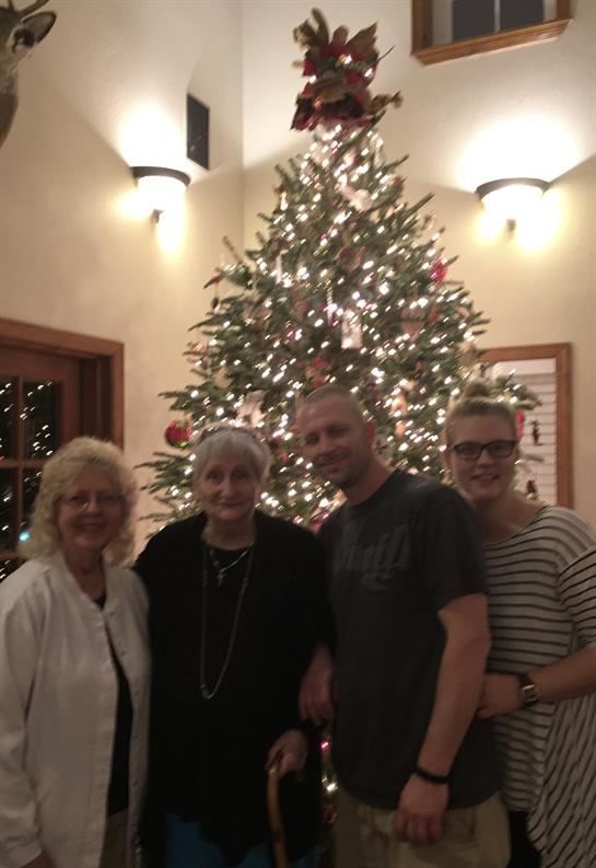 Family members pose together joyfully in front of a festive Christmas tree adorned with lights.