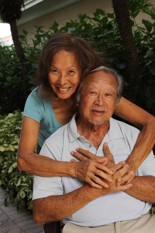 A happy elderly couple poses together, surrounded by vibrant plants and greenery.