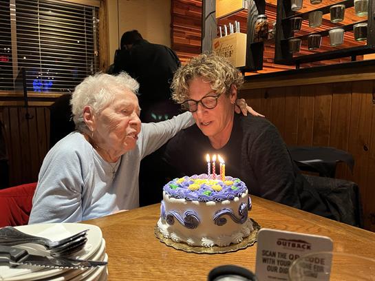 Two individuals sharing a heartfelt moment over a birthday cake with candles in a restaurant.