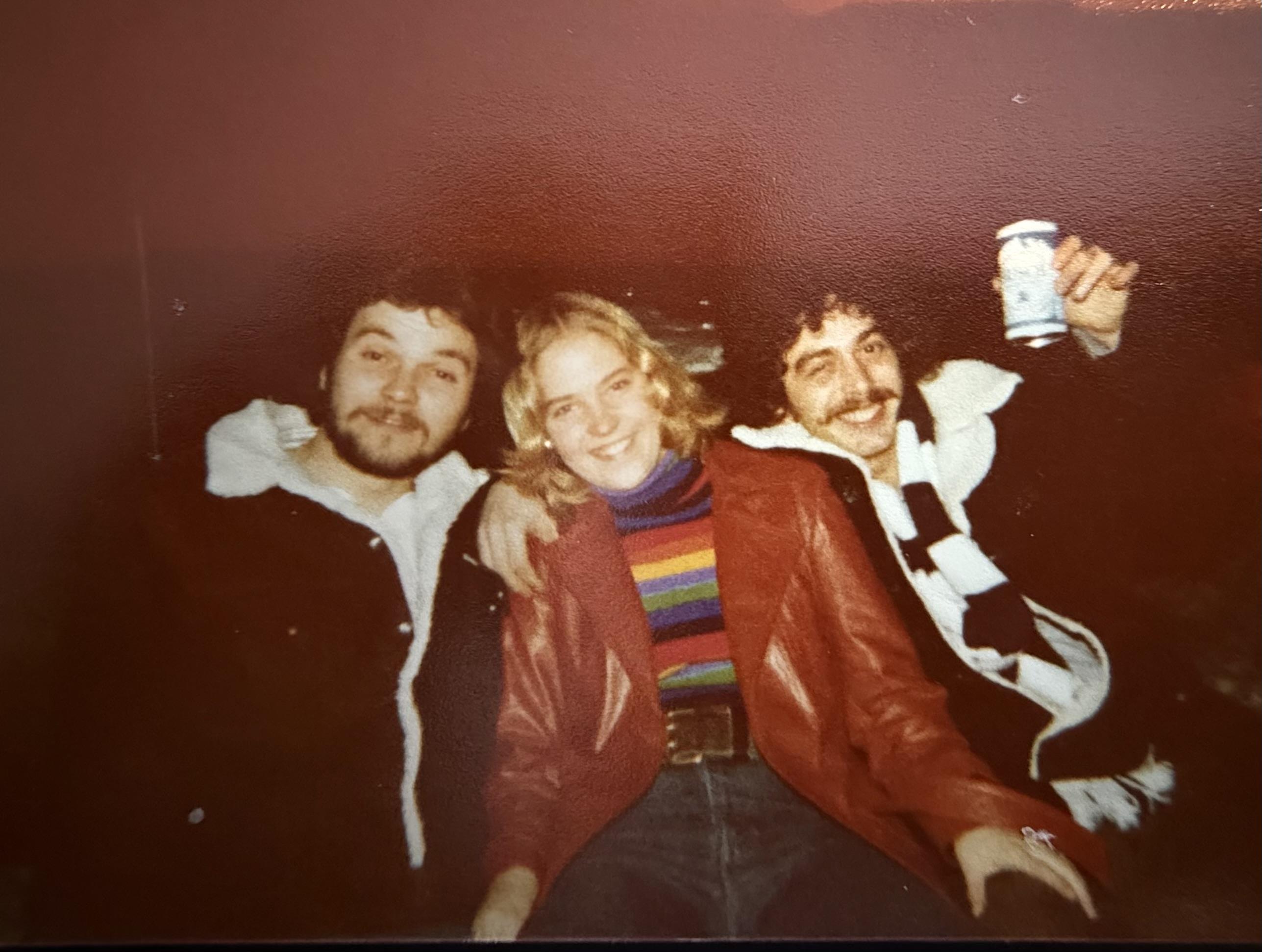Three friends share laughter and drinks during a fun outing at night in a casual environment.